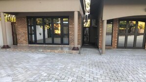 A building entrance with a paved walkway, a brick wall, and a glass door. - Makgadikgadi Riverview Inn (Nata)