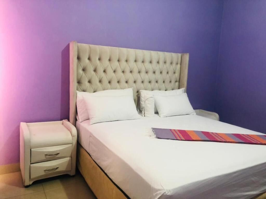 A bed with a tufted headboard, two pillows, a bedside table with drawers, and a colorful striped blanket.
