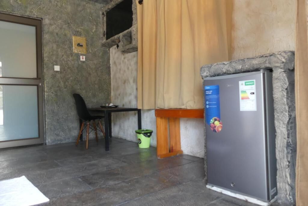 Une pièce avec un mur en pierre, une petite table avec une chaise, un réfrigérateur et une poubelle.