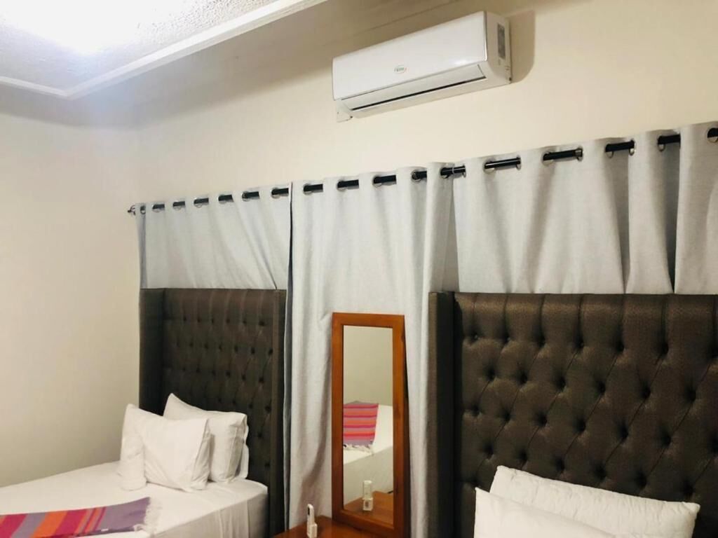 A hotel room with two beds, a mirror, an air conditioning unit, and a window with curtains.