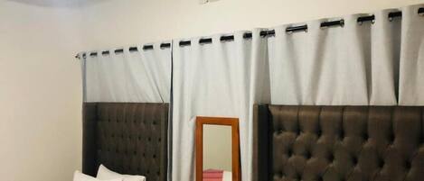 A hotel room with two beds, a mirror, an air conditioning unit, and a window with curtains.