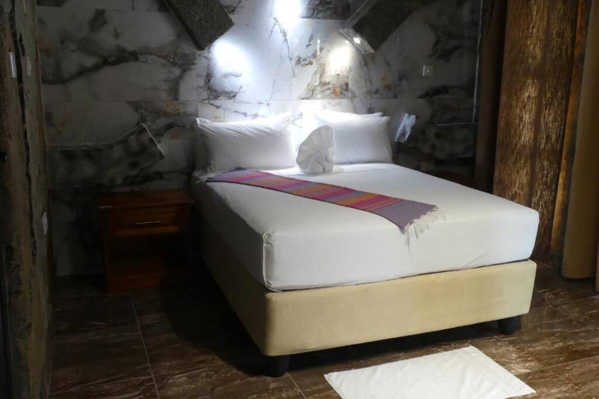 Un lit avec du linge de lit blanc, une table de chevet en bois et un mur décoré d’un motif imitant le marbre.