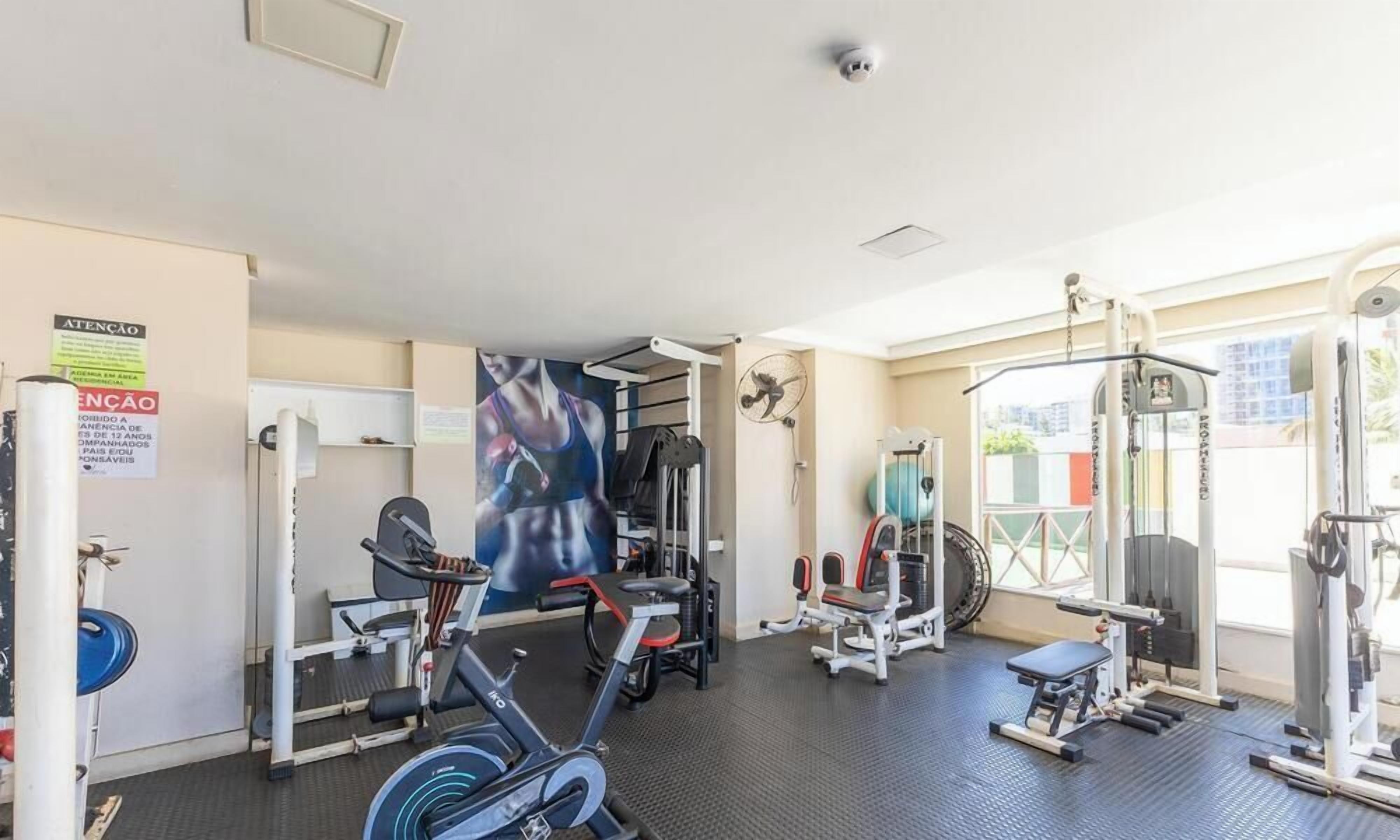 Un gimnasio con equipo de ejercicios, un ventilador en la pared y una puerta con un letrero.
