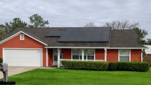 Une maison de plain-pied avec une façade rouge, une porte de garage blanche et un panneau solaire sur le toit.
