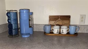 Un comptoir de cuisine avec une machine à café, une bouilloire et un plateau en bois contenant des tasses.