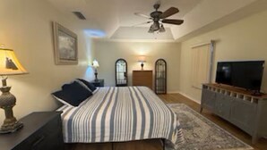 Une chambre à coucher comprenant un lit, des lampes de chevet, un ventilateur de plafond, une télévision et une commode.