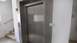 Un ascenseur moderne aux finitions métalliques, situé à côté d’un escalier doté d’une rampe.
