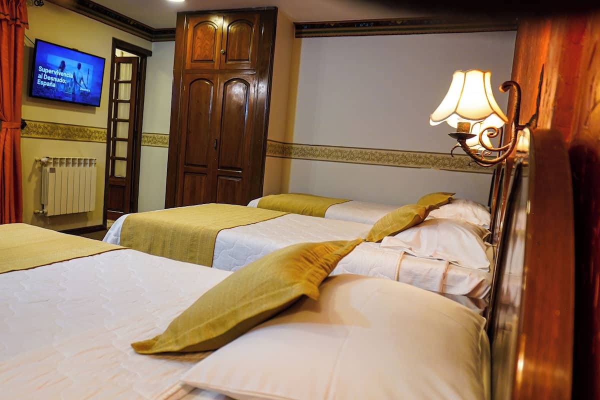 Una habitación de hotel con dos camas, televisión, armario de madera y lámpara.