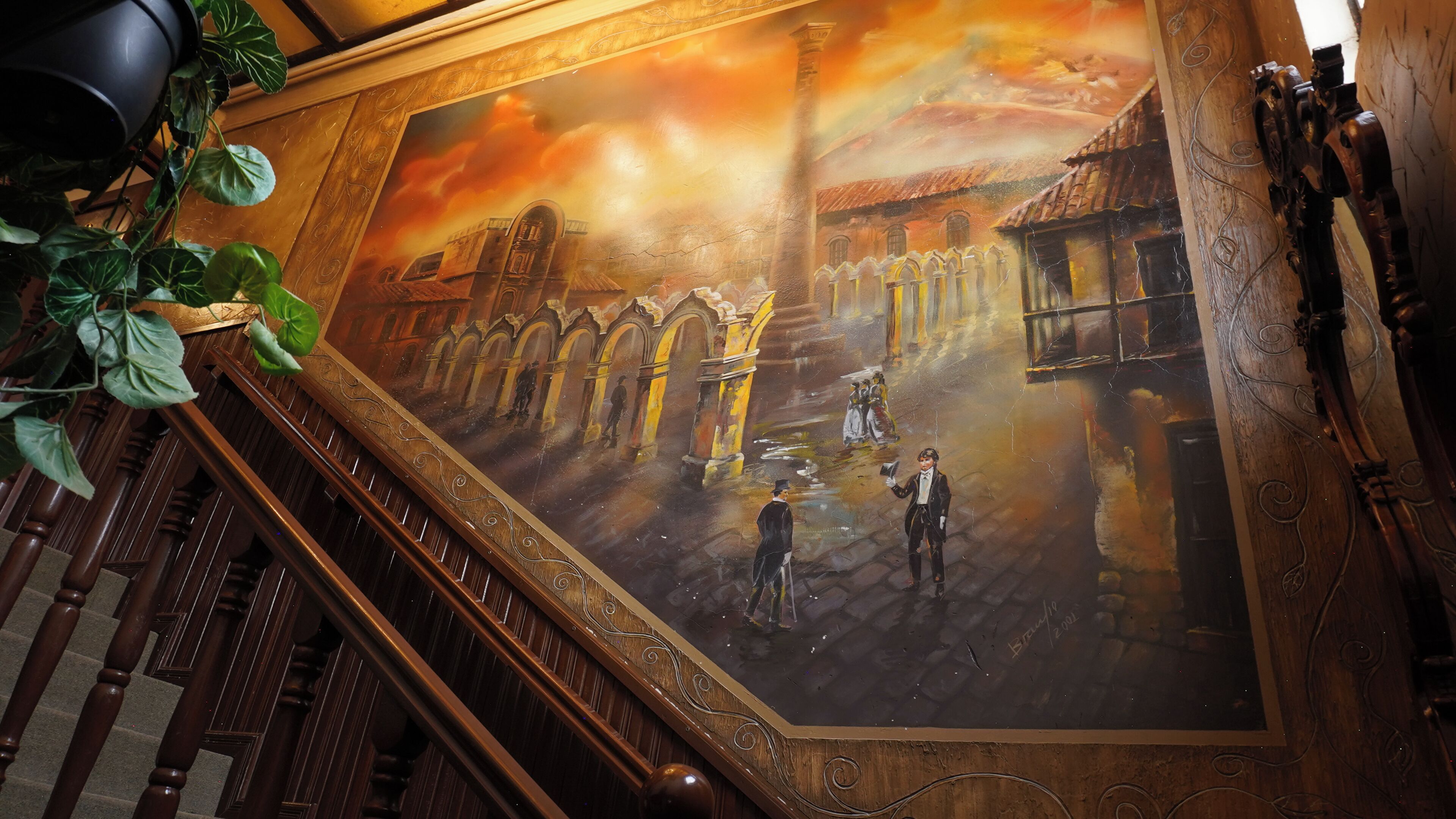 A mural of a street scene with buildings and people, a staircase with ornate woodwork, and a plant on the left.