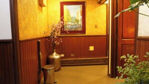 A hallway with a wooden door, a trash bin, a vase with flowers, and a framed painting on the wall. - Hostal Cerro Rico (Potosi)