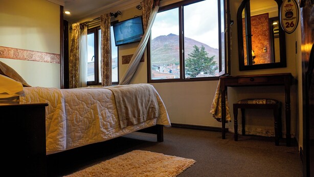 A bedroom with a bed, a TV, a window with a view of a mountain, and a fireplace. - Hostal Cerro Rico (Potosi)