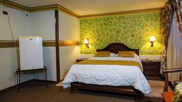 Habitación de hotel con cama, mesitas de noche, lámpara, teléfono y refrigerador.