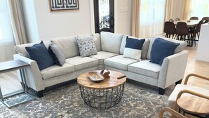 A modern living room with a beige sectional sofa, a round coffee table, and a patterned rug. - Stonewood Cottage  Magnolia/Baylor/Downtown Waco (Waco)