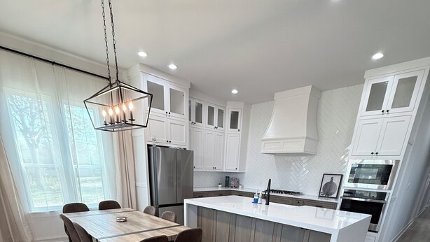 A modern kitchen with white cabinetry, a central island, and a dining area with a wooden table and chairs. - Stonewood Cottage  Magnolia/Baylor/Downtown Waco (Waco)