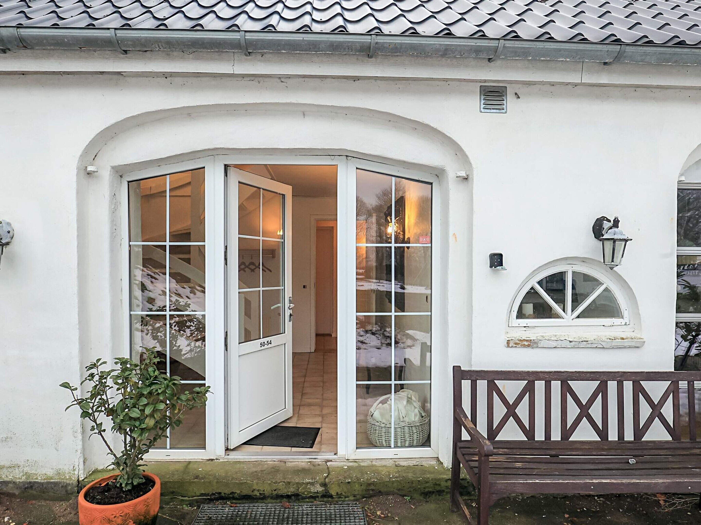 A white building with a white door and windows, a bench, and a potted plant.