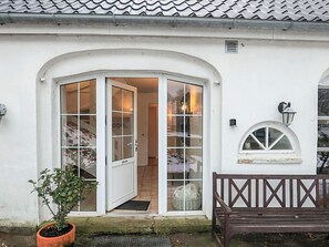 Ein weißes Gebäude mit weißer Tür und Fenstern, einer Bank und einem Blumentopf.