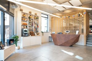 Un área de recepción moderna con un mostrador de madera, estanterías blancas con objetos decorativos y una escalera que conduce a un nivel superior.