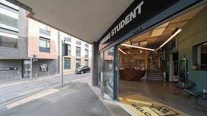 Entrada de um edifício moderno com a placa "CANVAS STUDENT", um tapete de boas-vindas e uma escadaria que dá acesso ao interior.