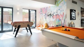 Uma mesa de bilhar com bolas, uma mesa de futebol de mesa e um muro com grafite colorido.