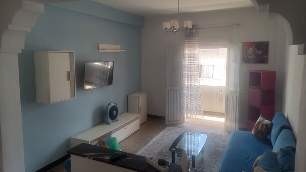 A living room with a blue sofa, a coffee table, a TV, and a fan. - Apartment center agdal (Rabat)