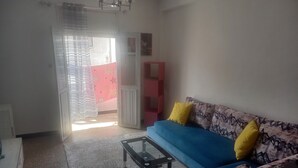 A living room with a blue sofa, yellow cushions, a glass coffee table, and a patterned rug. - Apartment center agdal (Rabat)