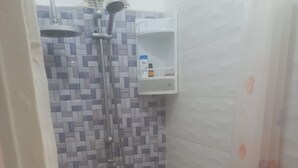 A small bathroom with a shower, a purple bucket, and a white shelf with toiletries. - Apartment center agdal (Rabat)