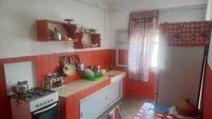 A kitchen with a gas stove, oven, and various utensils. There is a window with a checkered curtain and a tiled floor. - Apartment center agdal (Rabat)