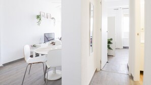 Una habitación moderna y minimalista con un escritorio blanco, una silla y una computadora. Hay cuadros enmarcados y una planta pequeña en la pared.