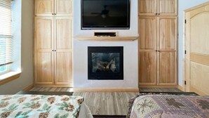 A room with a TV mounted above a fireplace, wooden cabinets, and a bed with a floral bedspread. - CBL 3306 (Brian Head)