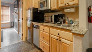 A compact kitchen with wooden cabinets, a stainless steel refrigerator, a microwave, and a dishwasher. - CBL 3306 (Brian Head)