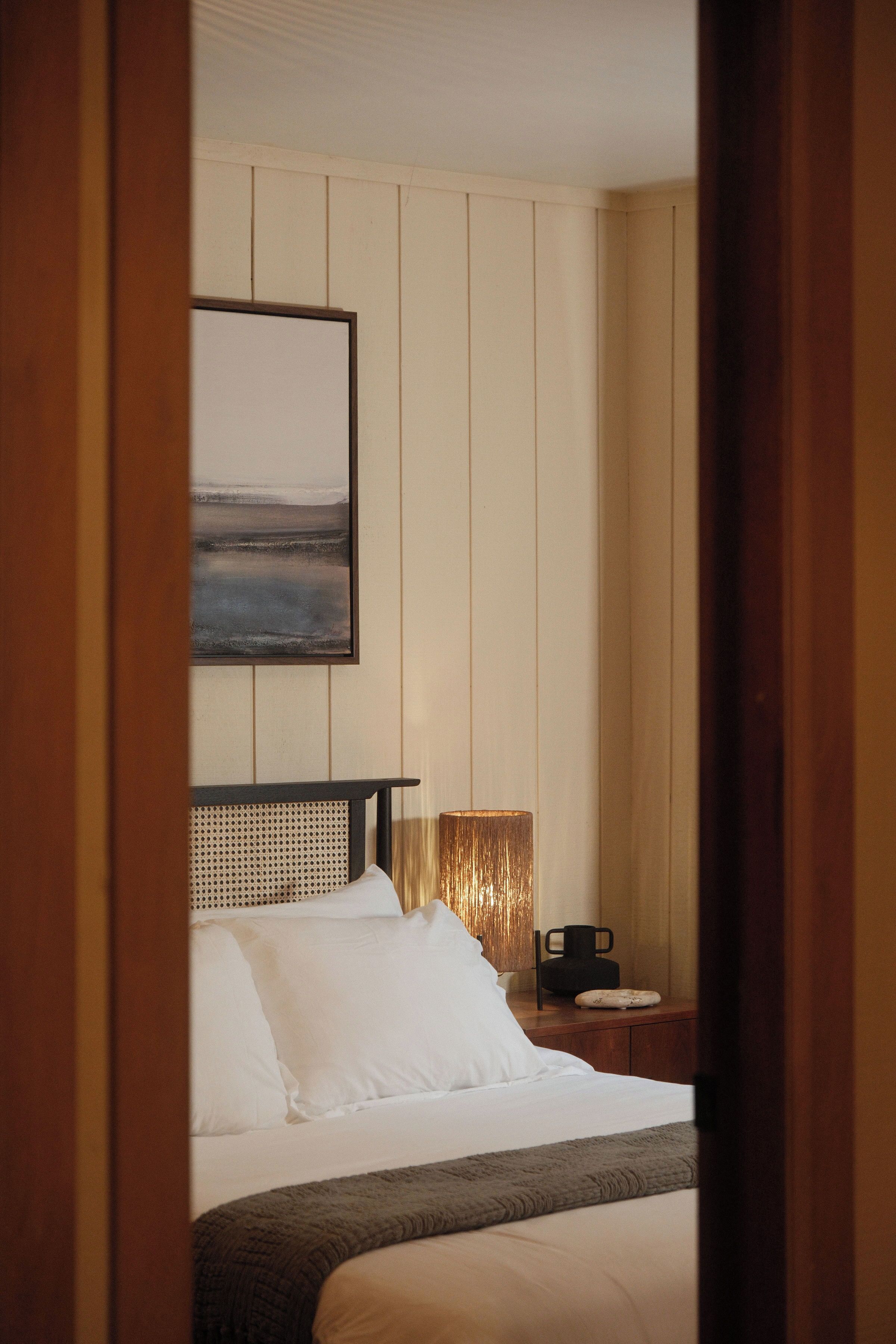 A hotel room with a bed, a bedside table, a lamp, and a painting on the wall.