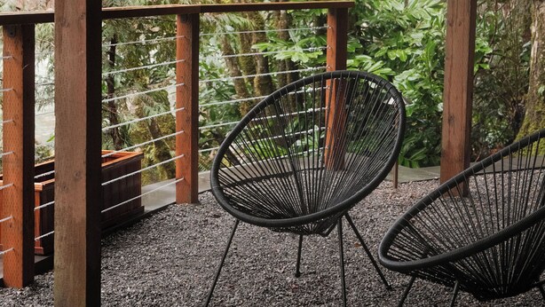 Area relax all'aperto, coperta, con due sedie in rete nera, travi in legno e vista su un giardino rigoglioso con alberi e piante.