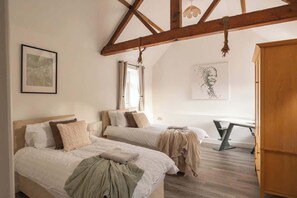 Ein Schlafzimmer mit zwei Betten, einer Holzbalkendecke, einem Schreibtisch und einem Fenster.