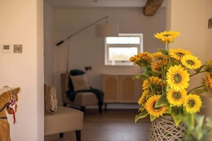 A living room with a sofa, a lamp, and a vase with sunflowers.