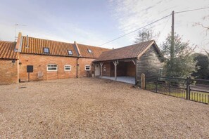A brick building with a gravel driveway and a wooden structure with a pitched roof.