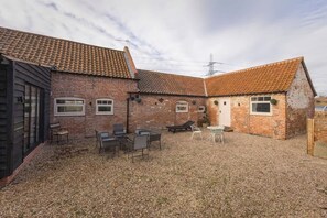 Ein Backsteinhaus mit Ziegeldach, einem Kieshof und Gartenmöbeln.