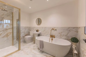 A modern bathroom with a freestanding bathtub, a glass-enclosed shower, a round mirror, and a small potted plant.