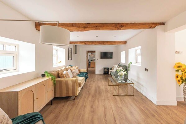A spacious living room with a wooden ceiling, a sofa set, a coffee table, and a TV mounted on the wall.