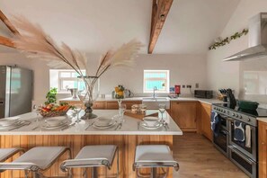 A modern kitchen with wooden cabinets, a central island with bar stools, a built-in oven, and a window providing natural light.