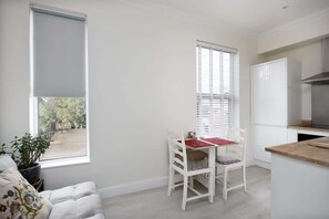A compact kitchen with white cabinets, a built-in oven, and a dining area with a table and chairs. - Immaculate Apartment | Historic Lincoln | Wi-Fi (Lincoln)