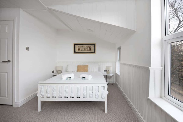 Serene bedroom with crisp white walls, a comfy double bed, and a cozy lounge chair for reading or relaxing. Enjoy your favorite shows on the TV, and let natural light fill the space through the window, creating a peaceful retreat after a busy day.