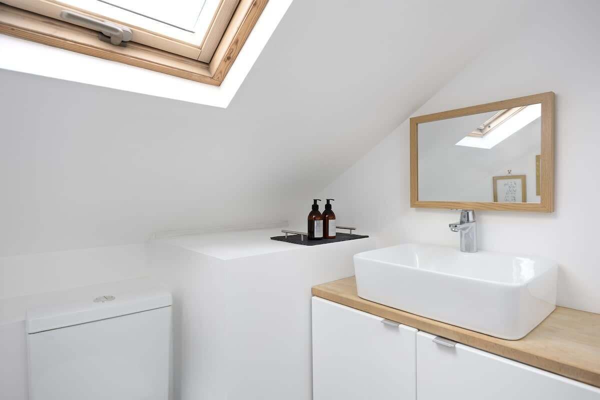 Une salle de bain moderne dotée d’un puits de lumière, d’un lavabo blanc et d’un plan de toilette en bois.