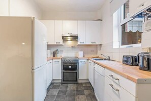 Une cuisine compacte avec des meubles blancs, un four encastré, un lave-vaisselle et une fenêtre au-dessus de l’évier.