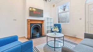 A living room with a fireplace, a Netflix sign, a blue sofa, a grey sofa, and a large window. - Perfect for Contractors | Central Location | Wi-Fi (Nottingham)