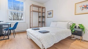 A bedroom with a bed, bedside table, chair, window, and a wooden shelf unit. - Perfect for Contractors | Central Location | Wi-Fi (Nottingham)