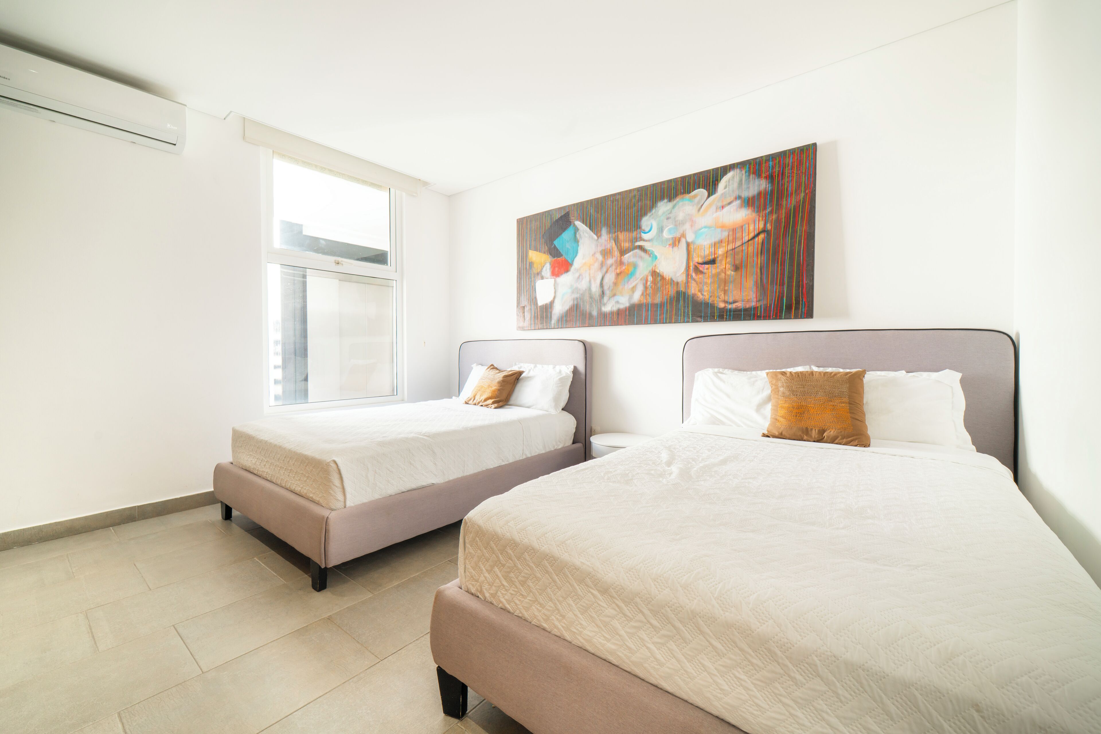 A hotel room with two beds, a large window, and a colorful abstract painting on the wall.