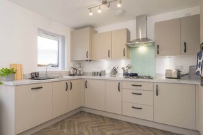 A modern kitchen with light-colored cabinets, a stainless steel range hood, and a window providing natural light. - Cosy Home | Parking | Royal Derby Hospital (Derby)