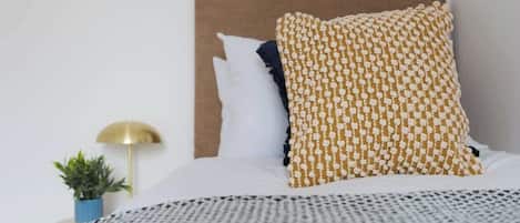A neatly made bed with patterned pillows, a small bedside plant, and a wall-mounted lamp.