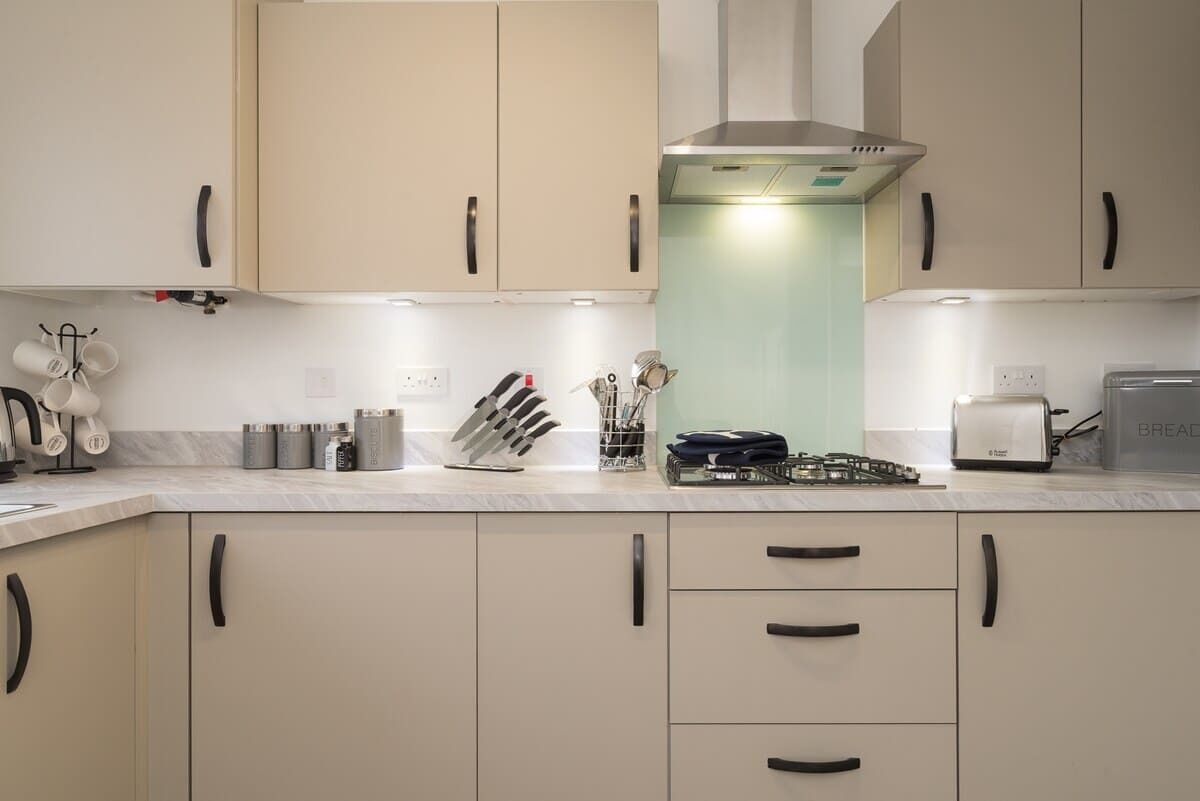 Een moderne keuken met beige kastjes, een roestvrijstalen afzuigkap en diverse keukengerei.
