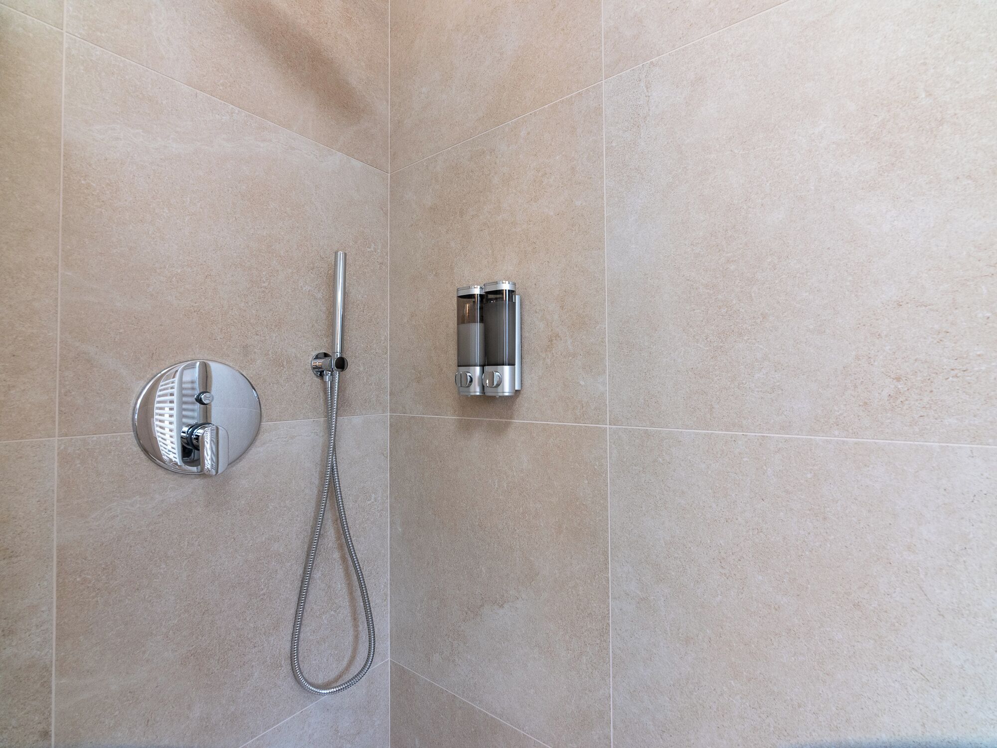 Un baño con ducha, un cabezal de ducha manual y un panel de control en la pared.